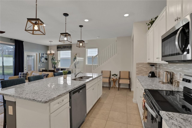 kitchen with an island with sink, hanging light fixtures, backsplash, stainless steel appliances, and white cabinetry