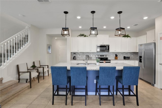 kitchen featuring a kitchen island with sink, sink, white cabinets, stainless steel appliances, and tasteful backsplash