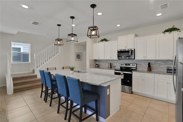 kitchen featuring white cabinets, appliances with stainless steel finishes, tasteful backsplash, and an island with sink