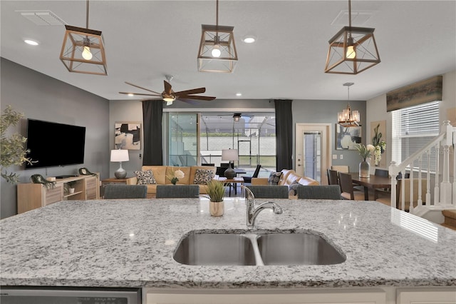 kitchen with light stone counters, a healthy amount of sunlight, ceiling fan with notable chandelier, and sink