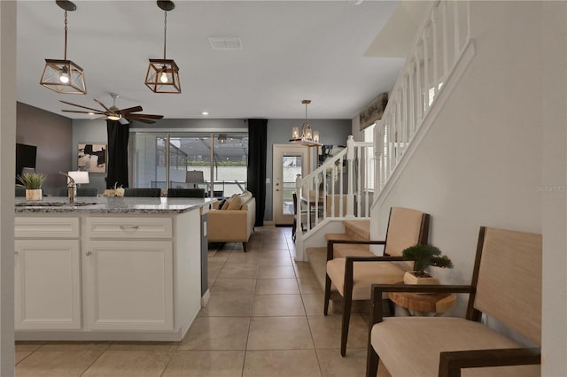 kitchen with hanging light fixtures, ceiling fan with notable chandelier, light tile floors, white cabinets, and light stone counters