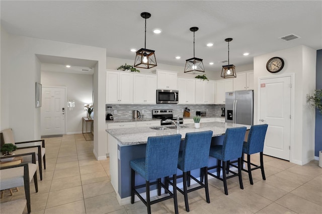 kitchen featuring pendant lighting, a center island with sink, stainless steel appliances, tasteful backsplash, and white cabinetry