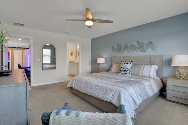 bedroom with ensuite bathroom, light colored carpet, and ceiling fan