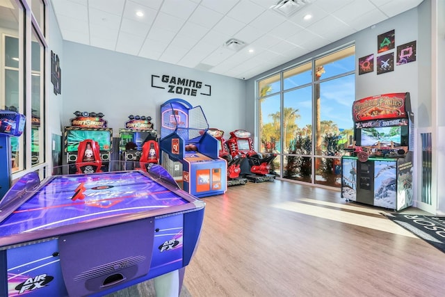 game room with floor to ceiling windows, light hardwood / wood-style floors, and a drop ceiling