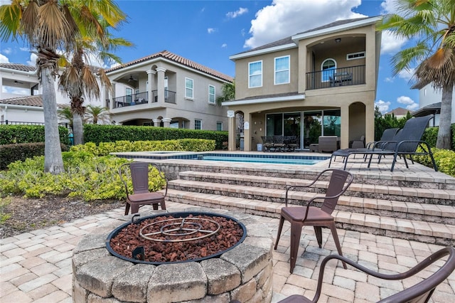 back of property featuring a balcony, a fire pit, and a patio