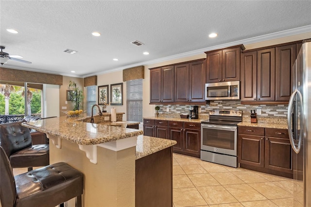 kitchen with appliances with stainless steel finishes, light stone counters, light tile floors, ceiling fan, and a kitchen breakfast bar