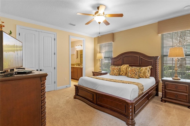 carpeted bedroom with a closet, ensuite bath, ceiling fan, and ornamental molding