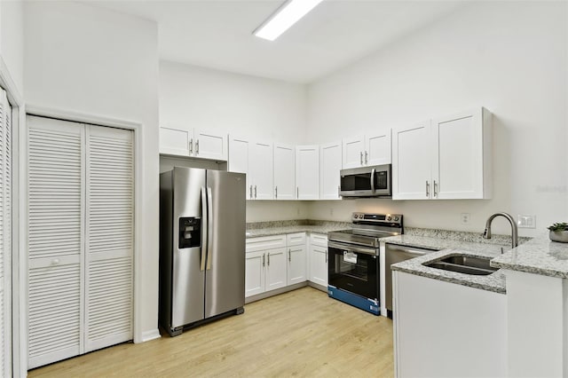 kitchen with white cabinets, sink, light hardwood / wood-style flooring, light stone countertops, and appliances with stainless steel finishes