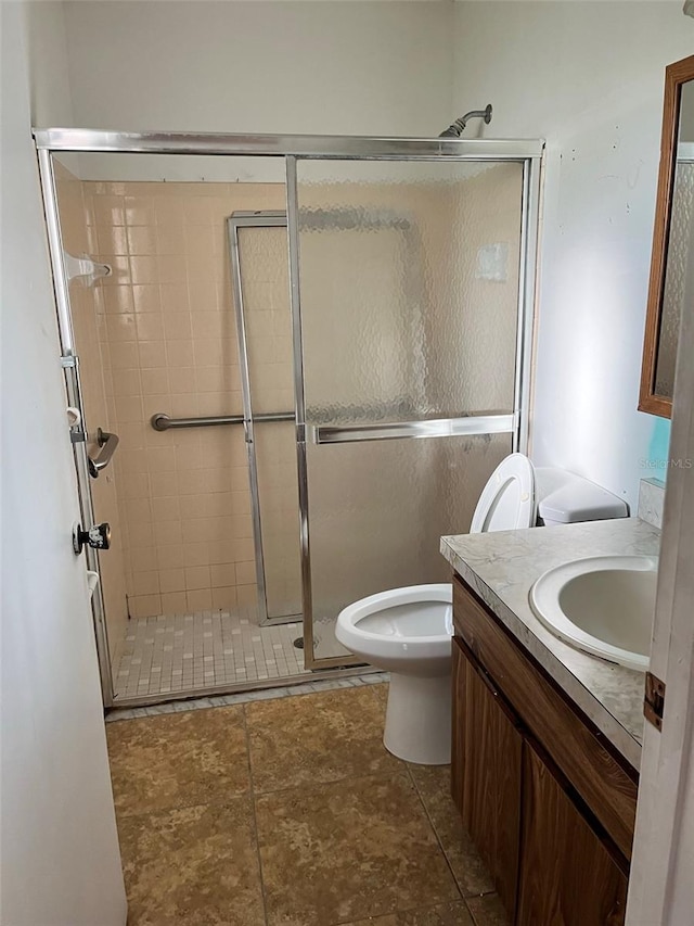 bathroom with tile floors, toilet, vanity, and a shower with shower door