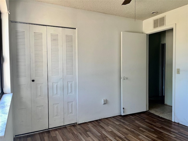 unfurnished bedroom featuring a closet, a textured ceiling, visible vents, and dark wood-style flooring