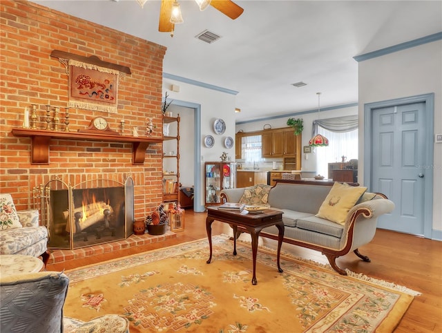 living room with brick wall, a brick fireplace, light hardwood / wood-style floors, and ceiling fan