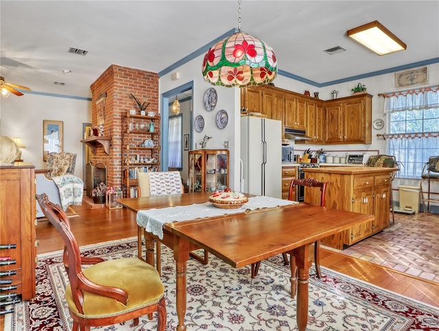 dining space with brick wall, ornamental molding, a fireplace, and ceiling fan