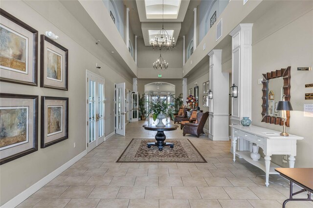 interior space with a notable chandelier, french doors, decorative columns, and a towering ceiling