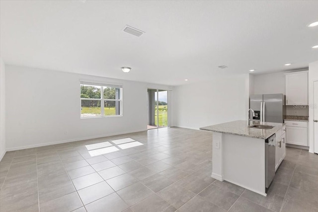 kitchen featuring a center island with sink, light stone counters, white cabinetry, and appliances with stainless steel finishes