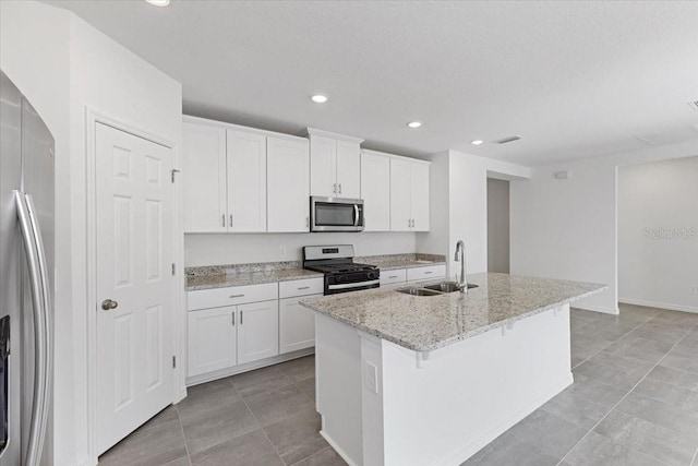 kitchen with white cabinets, sink, light stone countertops, an island with sink, and appliances with stainless steel finishes