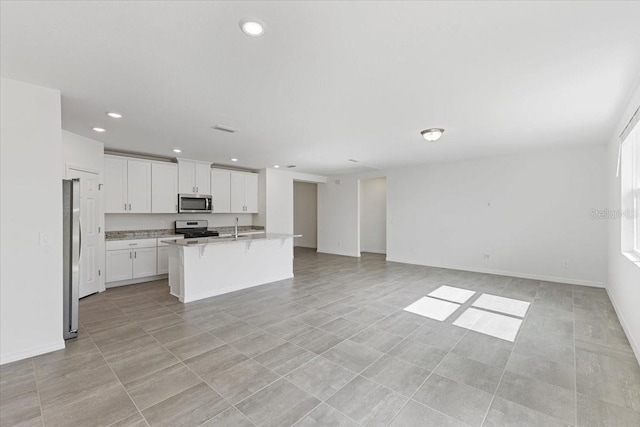 kitchen with white cabinetry, a center island with sink, stainless steel appliances, and light stone counters