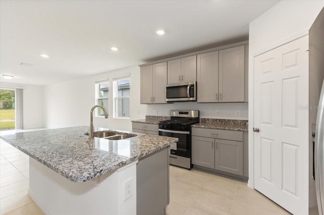 kitchen featuring gray cabinetry, stainless steel appliances, light tile floors, sink, and an island with sink