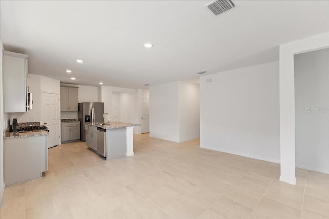 kitchen with sink, light tile flooring, stainless steel appliances, a center island with sink, and light stone countertops