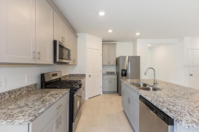 kitchen featuring appliances with stainless steel finishes, light tile floors, sink, gray cabinetry, and an island with sink