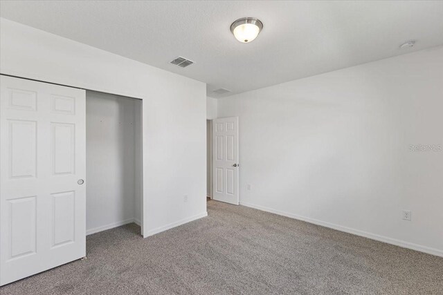 unfurnished bedroom featuring carpet floors, a textured ceiling, and a closet