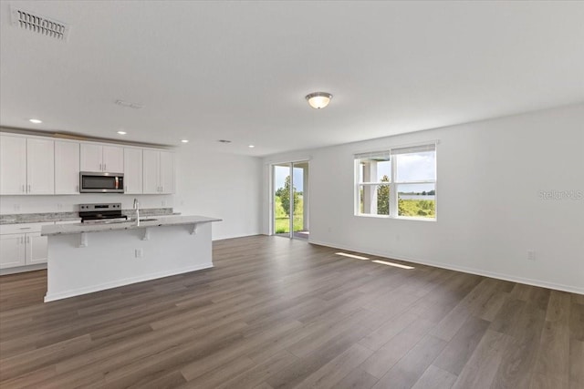 kitchen with a kitchen bar, white cabinetry, light stone counters, appliances with stainless steel finishes, and an island with sink