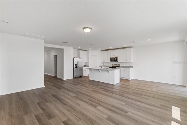 kitchen with light hardwood / wood-style flooring, white cabinetry, stainless steel appliances, a kitchen breakfast bar, and a center island with sink