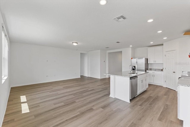 kitchen with light wood-type flooring, an island with sink, white cabinets, and appliances with stainless steel finishes