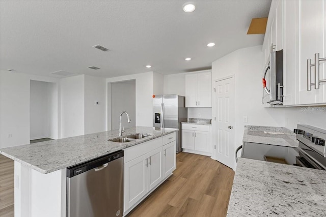 kitchen featuring sink, a center island with sink, appliances with stainless steel finishes, light stone countertops, and white cabinets