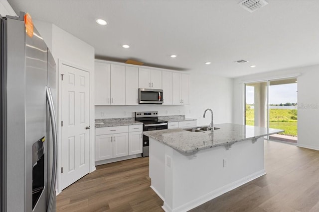 kitchen featuring sink, appliances with stainless steel finishes, a kitchen island with sink, light stone countertops, and white cabinets