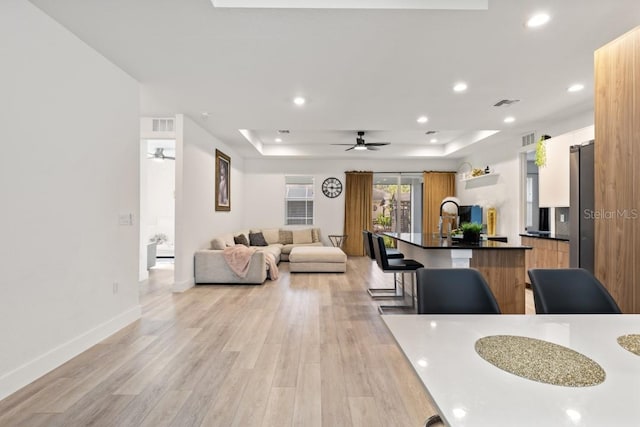 interior space with ceiling fan, a tray ceiling, and light hardwood / wood-style flooring