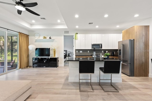 kitchen with stainless steel appliances, ceiling fan, tasteful backsplash, white cabinets, and a tray ceiling