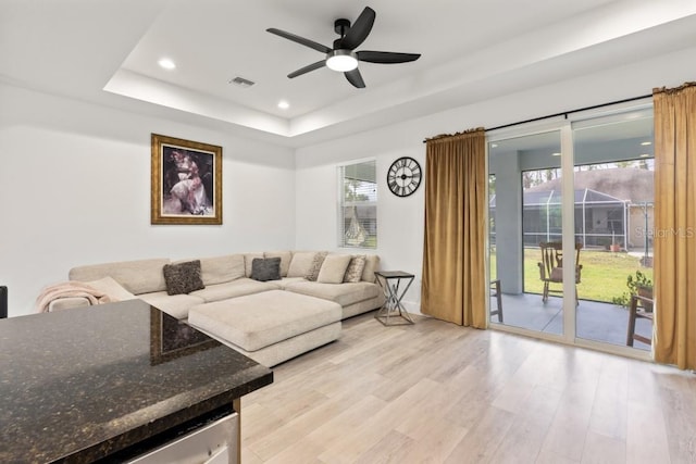 living room featuring a raised ceiling, ceiling fan, and light wood-type flooring