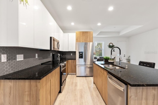 kitchen with sink, stainless steel appliances, tasteful backsplash, white cabinetry, and light wood-type flooring