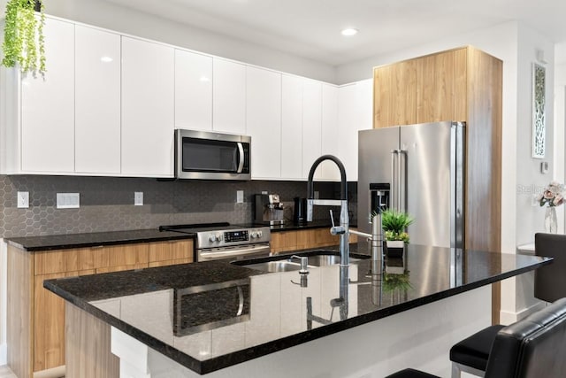 kitchen with backsplash, dark stone countertops, appliances with stainless steel finishes, and white cabinetry