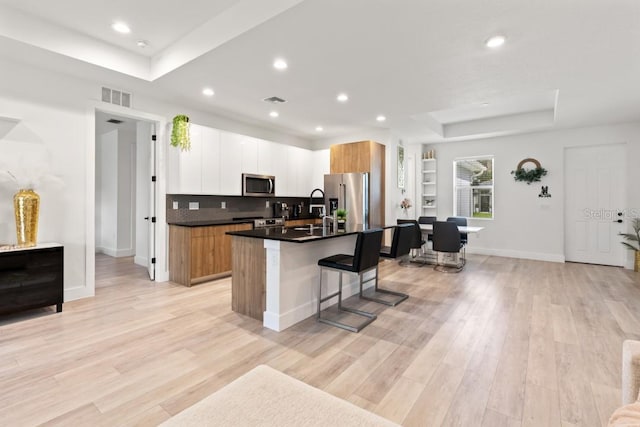 kitchen with a raised ceiling, stainless steel appliances, white cabinets, and light wood-type flooring