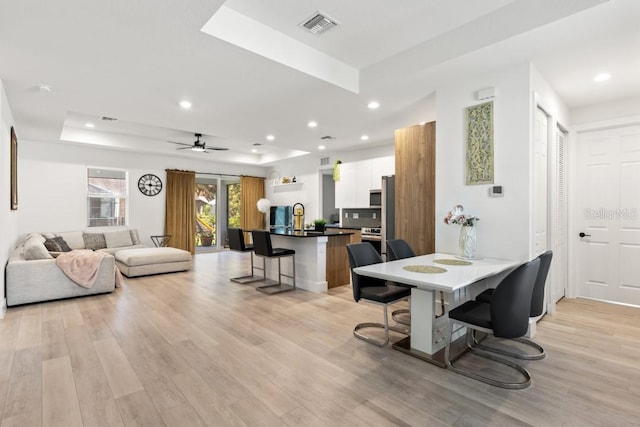 dining area with ceiling fan, a raised ceiling, and light hardwood / wood-style flooring