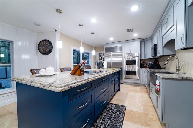 kitchen featuring appliances with stainless steel finishes, pendant lighting, light stone countertops, a center island with sink, and light tile patterned floors