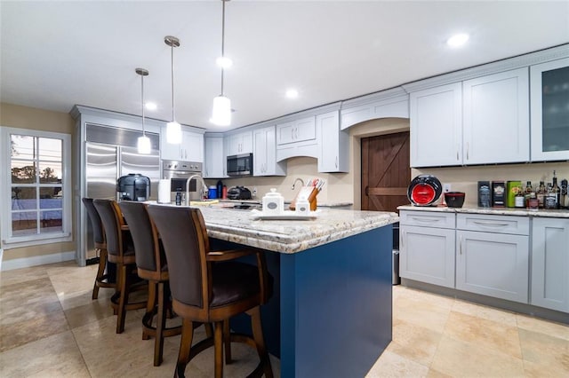 kitchen featuring light stone countertops, appliances with stainless steel finishes, a kitchen island with sink, and decorative light fixtures