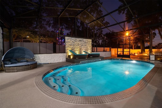 pool at night featuring a hot tub, glass enclosure, and a patio