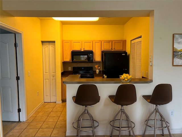 kitchen featuring a breakfast bar, a peninsula, light tile patterned flooring, black appliances, and backsplash