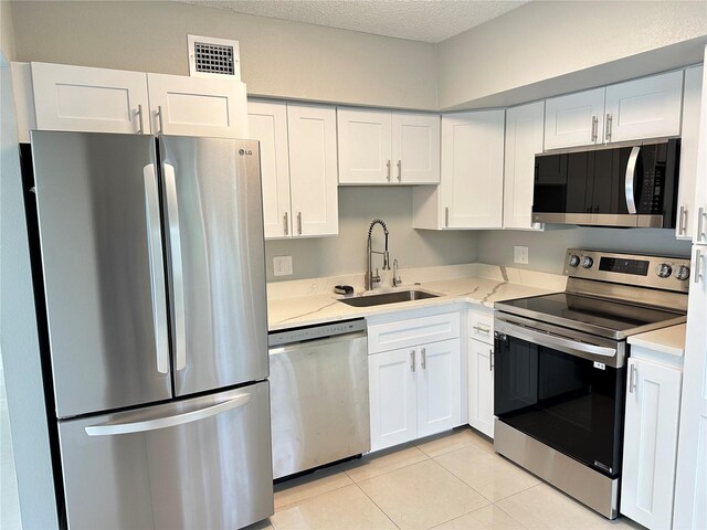 kitchen with appliances with stainless steel finishes, sink, a textured ceiling, white cabinetry, and light tile patterned floors