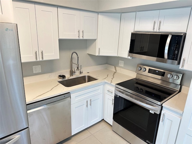 kitchen with light stone countertops, appliances with stainless steel finishes, sink, white cabinets, and light tile patterned floors