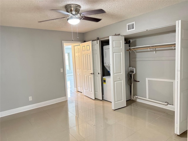 unfurnished bedroom with light tile patterned flooring, a barn door, a textured ceiling, ceiling fan, and stacked washer and clothes dryer