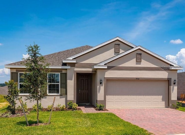 ranch-style home with stucco siding, decorative driveway, a front yard, and an attached garage