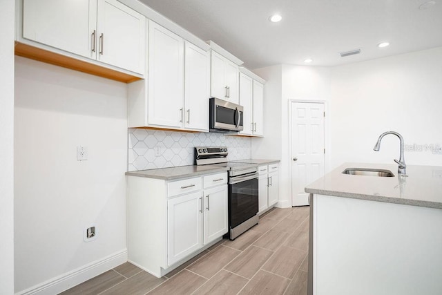 kitchen with tasteful backsplash, stainless steel appliances, light stone counters, sink, and white cabinetry