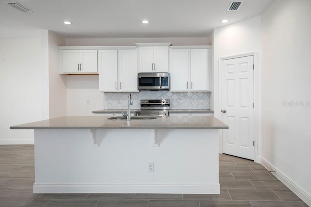 kitchen with white cabinets, an island with sink, appliances with stainless steel finishes, and decorative backsplash