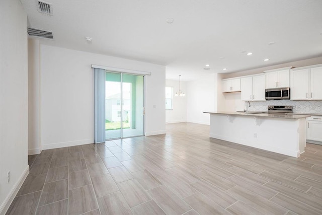 kitchen with a kitchen island with sink, stainless steel appliances, sink, tasteful backsplash, and white cabinets