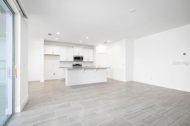 kitchen featuring a center island with sink, stainless steel appliances, a breakfast bar, tasteful backsplash, and white cabinets