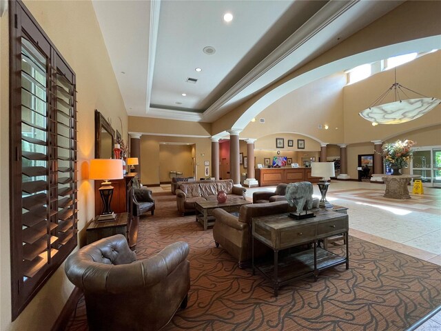 tiled living room featuring a raised ceiling, a chandelier, ornate columns, and a towering ceiling