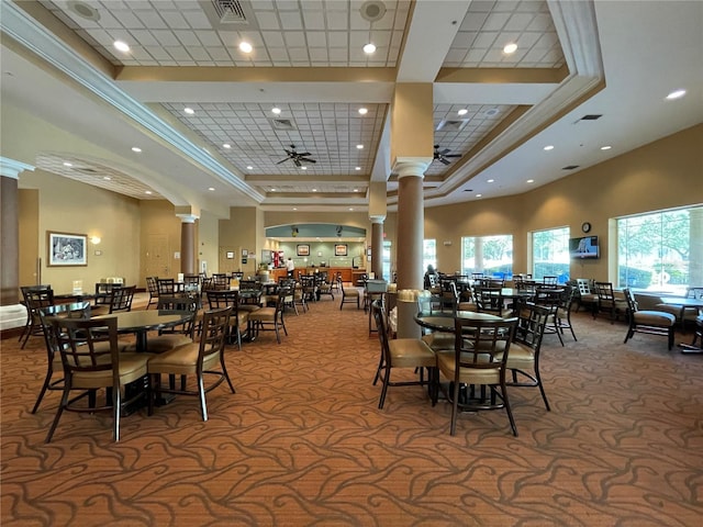 dining room featuring ceiling fan, a towering ceiling, a raised ceiling, ornate columns, and carpet floors